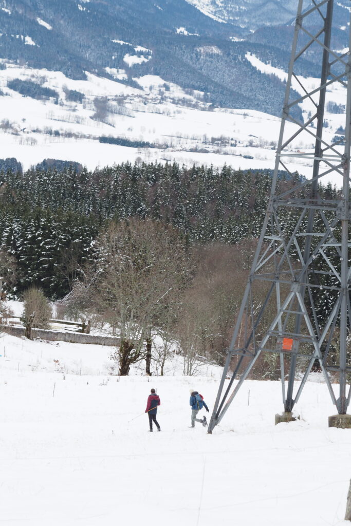 Un pylône électrique auprès duquel courent deux personnes en raquettes dans la neige